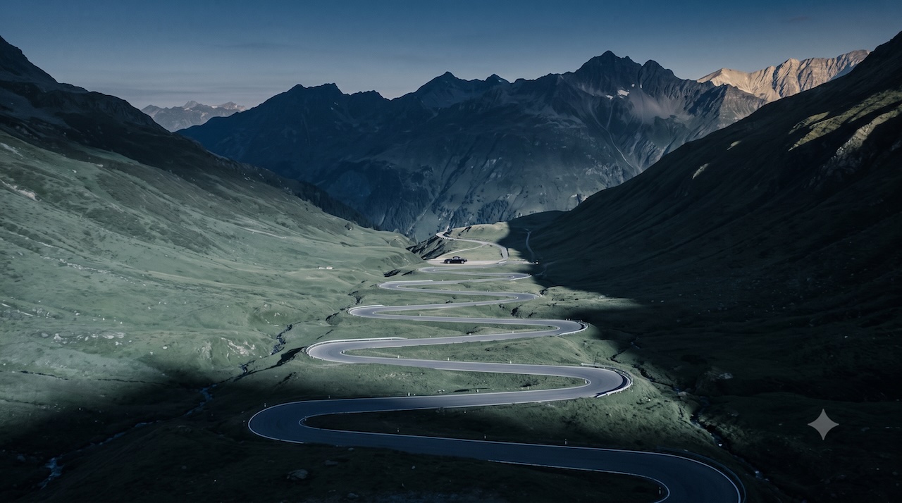 Eine leere Passstrasse in Kehren im Morgenlicht, ein einzelner Wagen weit in der Ferne.